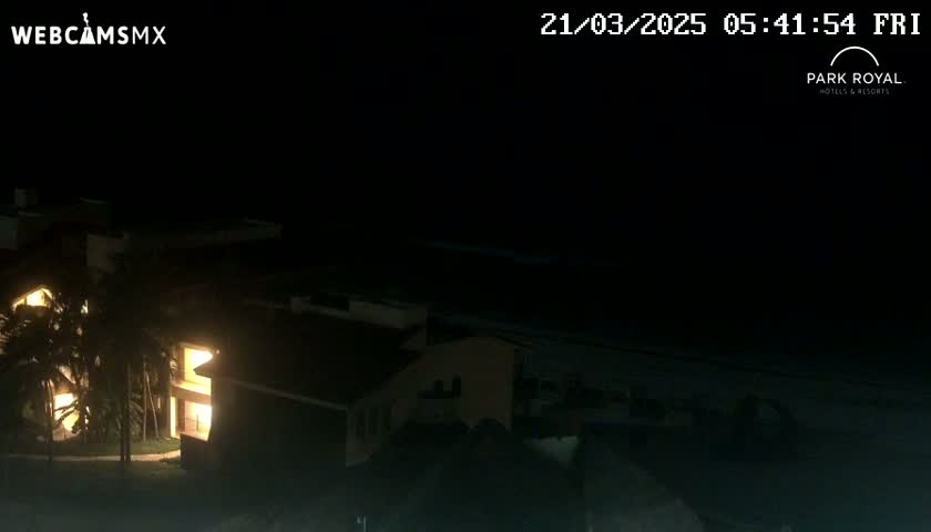 A nighttime view shows illuminated buildings near a dark body of water under a clear, dark sky.