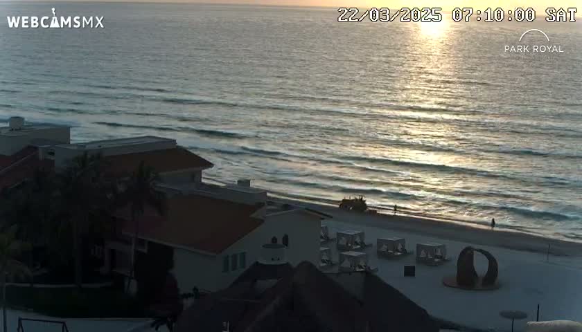 A sunrise illuminates the ocean waves as they lap a sandy beach near a beachfront building complex.