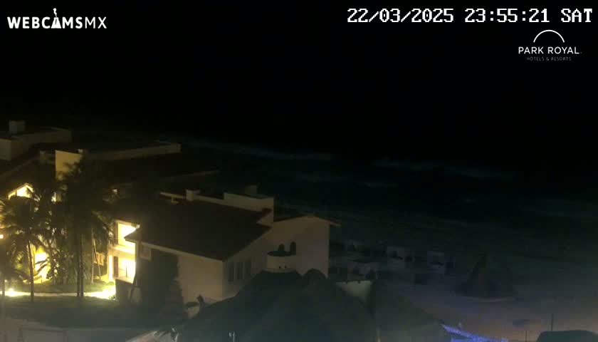 A nighttime view of a brightly lit building complex overlooking a dark ocean with gentle waves under a clear sky.