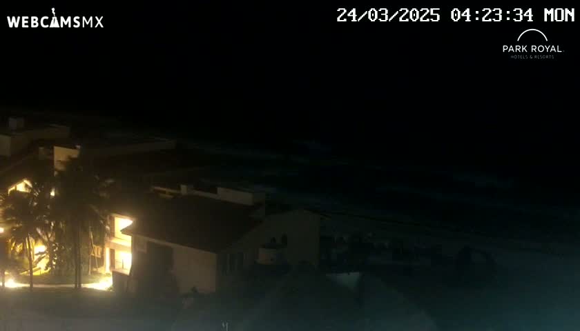 A nighttime view of a brightly lit building complex next to a dark ocean under a clear sky.