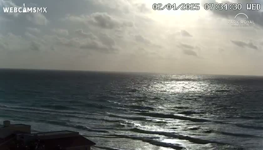 A partly cloudy sky over a dark-blue ocean with small waves reflecting sunlight.