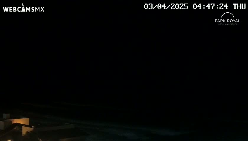 A dark nighttime scene shows a body of water and dimly lit buildings along the shoreline.