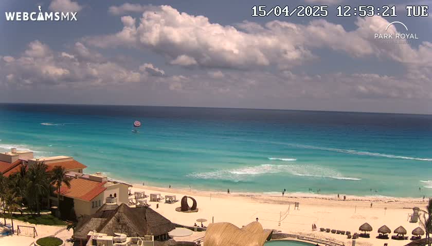 A partly cloudy day shows a beach with turquoise water,  buildings, and people enjoying the sand and ocean.