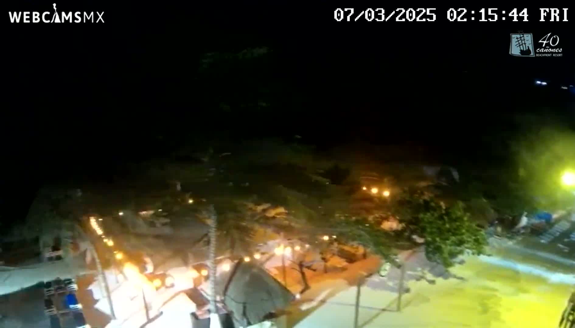 A nighttime, aerial view of a beachside resort with lights illuminating the buildings and surrounding area.