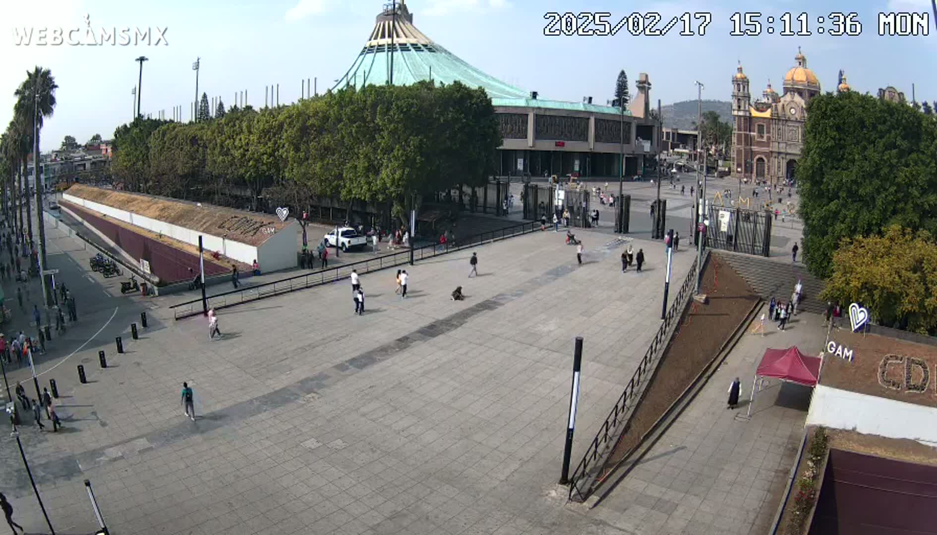 A large plaza with scattered people is seen in front of a basilica and a modern building under a mostly sunny sky.