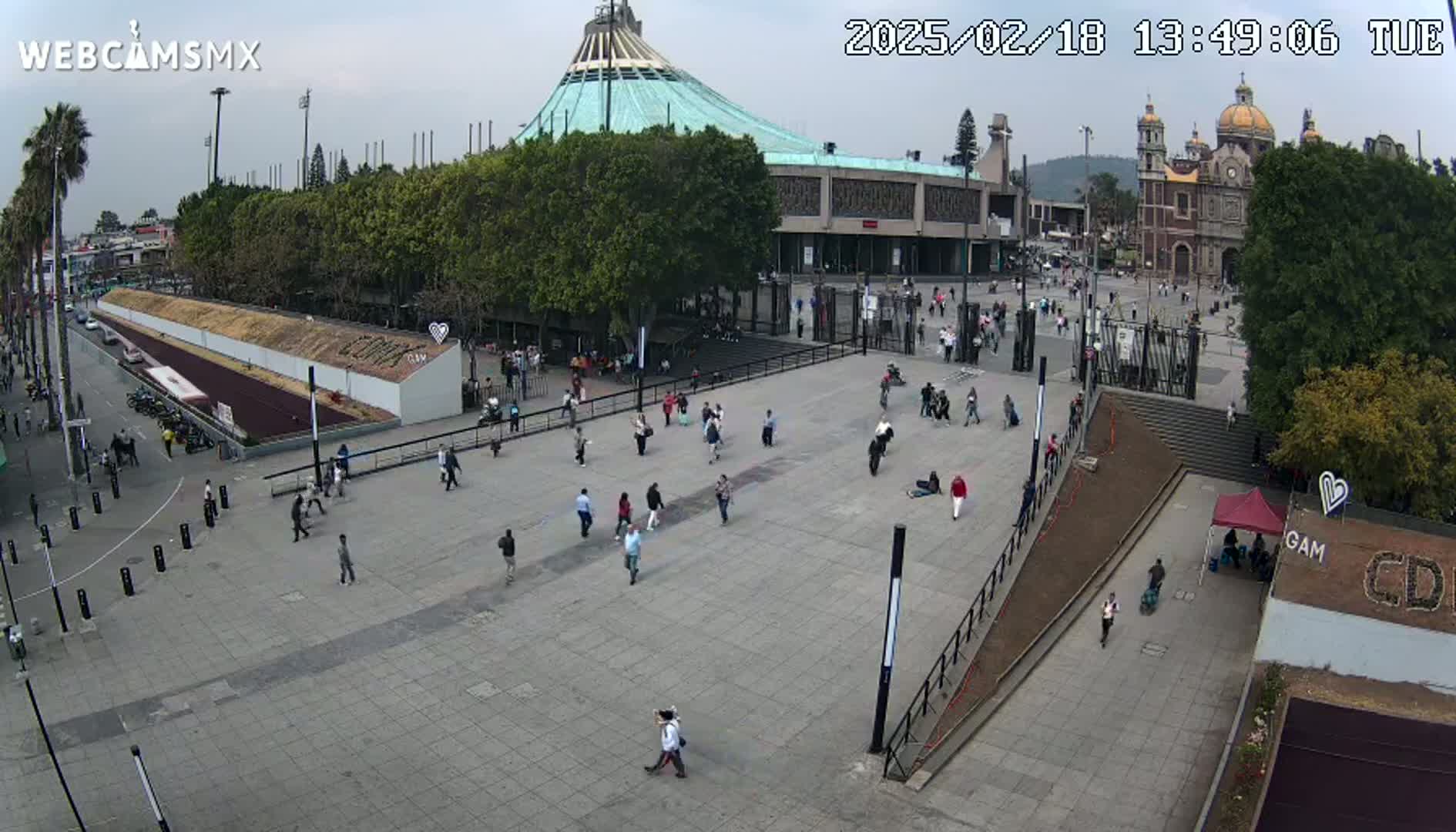 A large plaza with scattered people, a basilica, and a modern building under a mostly cloudy sky.