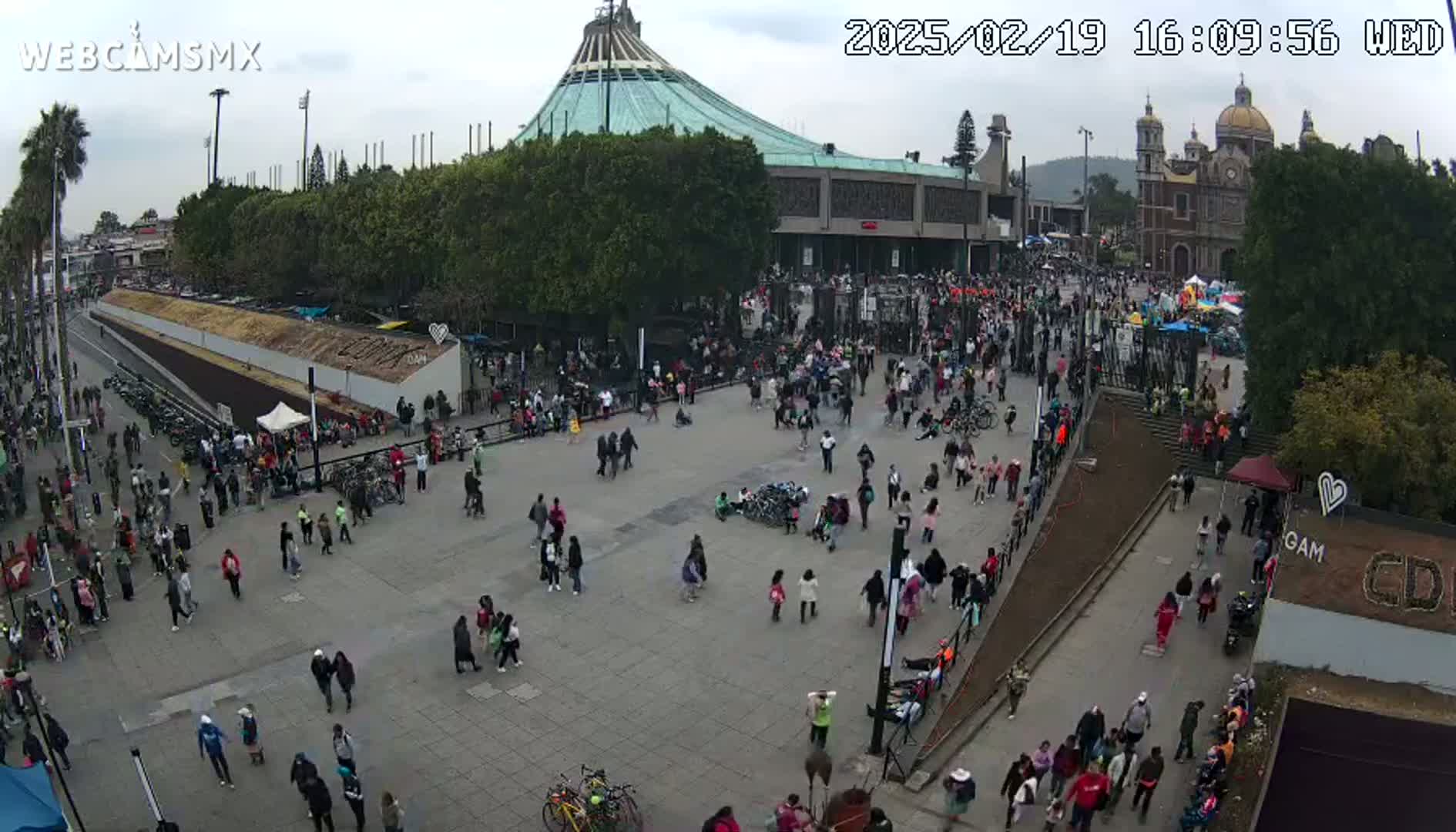 A large crowd of people gathers in a plaza in front of a basilica on an overcast day.