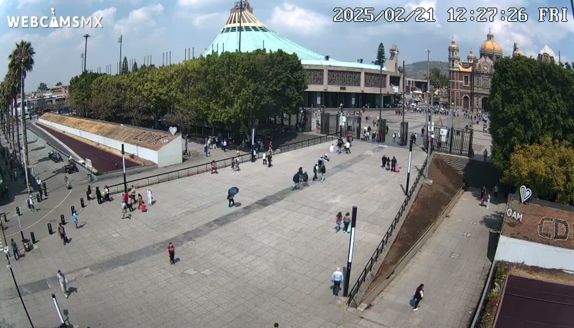 A large plaza with a few people walking around, in front of a large basilica under a mostly sunny sky.