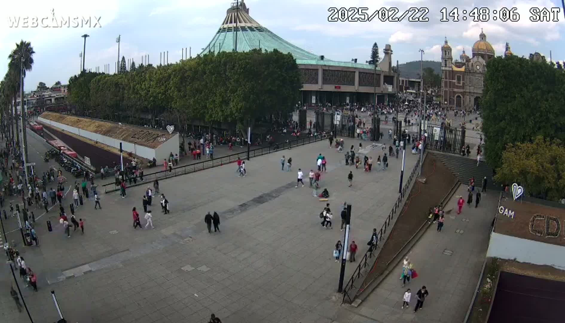A large plaza with many people is seen in front of a basilica on a partly cloudy day.