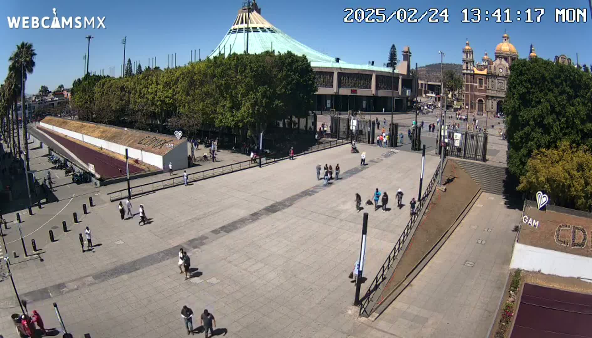 A large plaza with a few people walking around, in front of a basilica and a large building under a sunny sky.