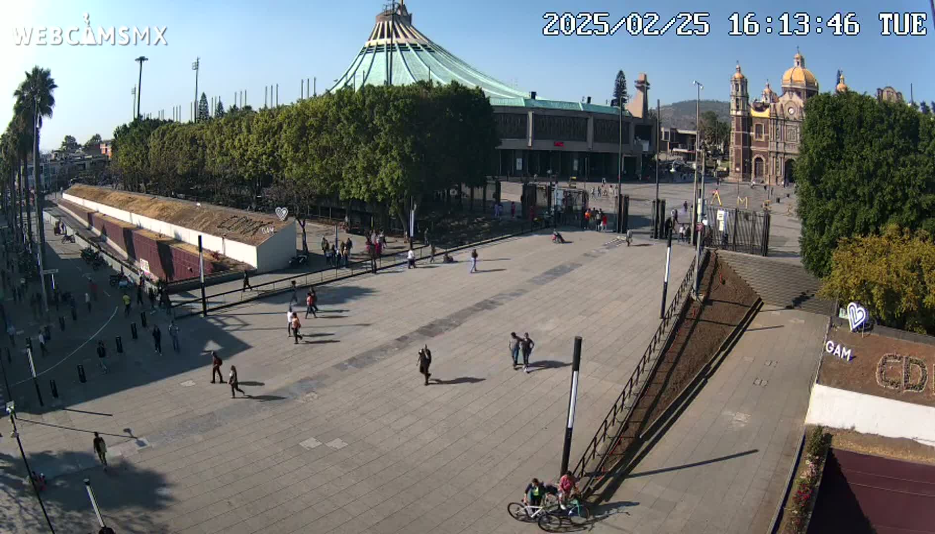 A large plaza with a few people walking around, a large basilica in the background, and a clear sunny day.