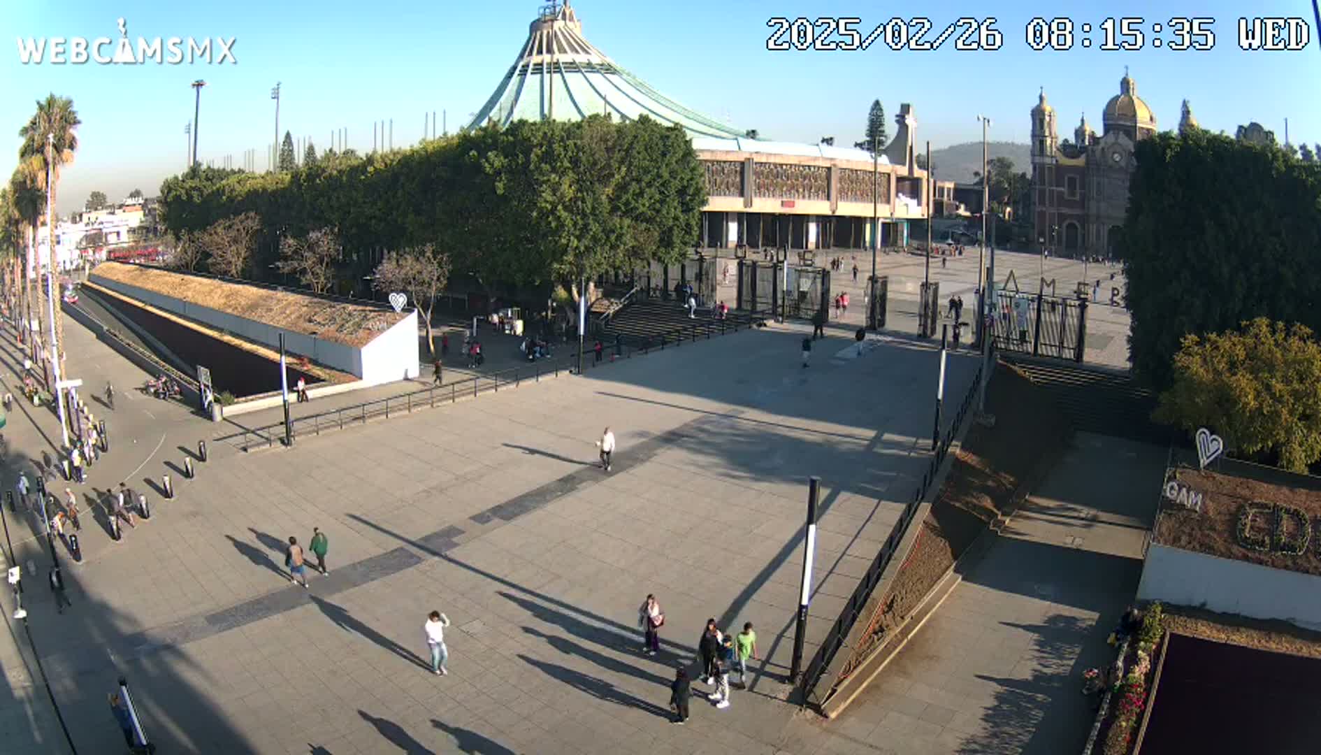 A large plaza with a few people walking around, in front of a large basilica and smaller church under a sunny sky.
