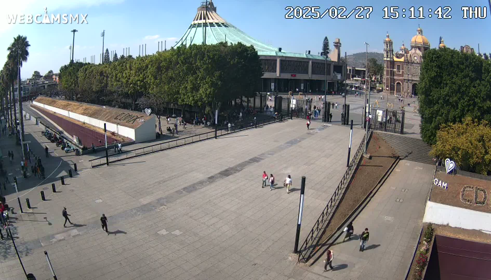 A large plaza with several people walking, situated between two large religious buildings under a clear, sunny sky.