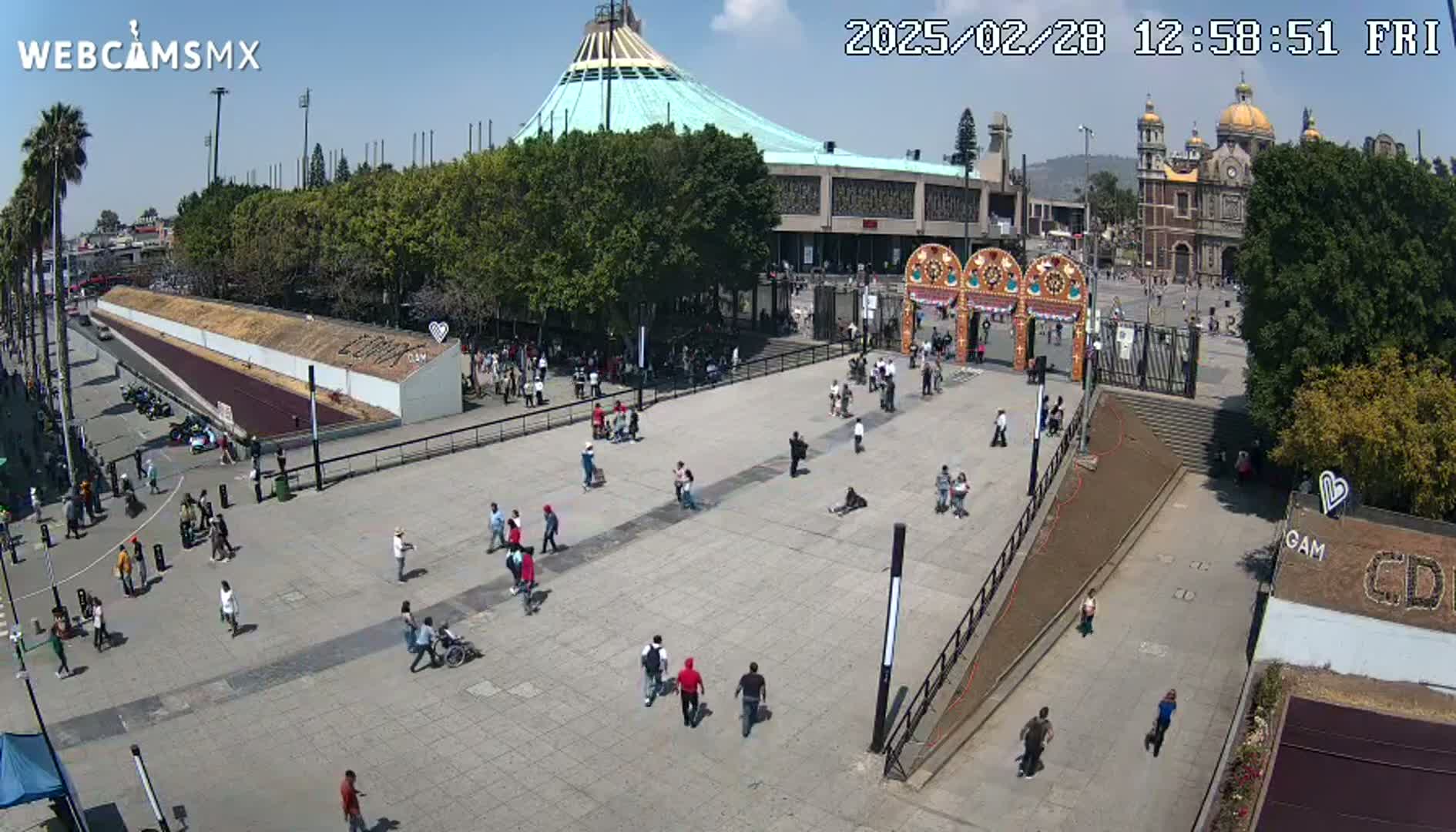 A large plaza with numerous people, a basilica, and a modern building under a sunny sky.