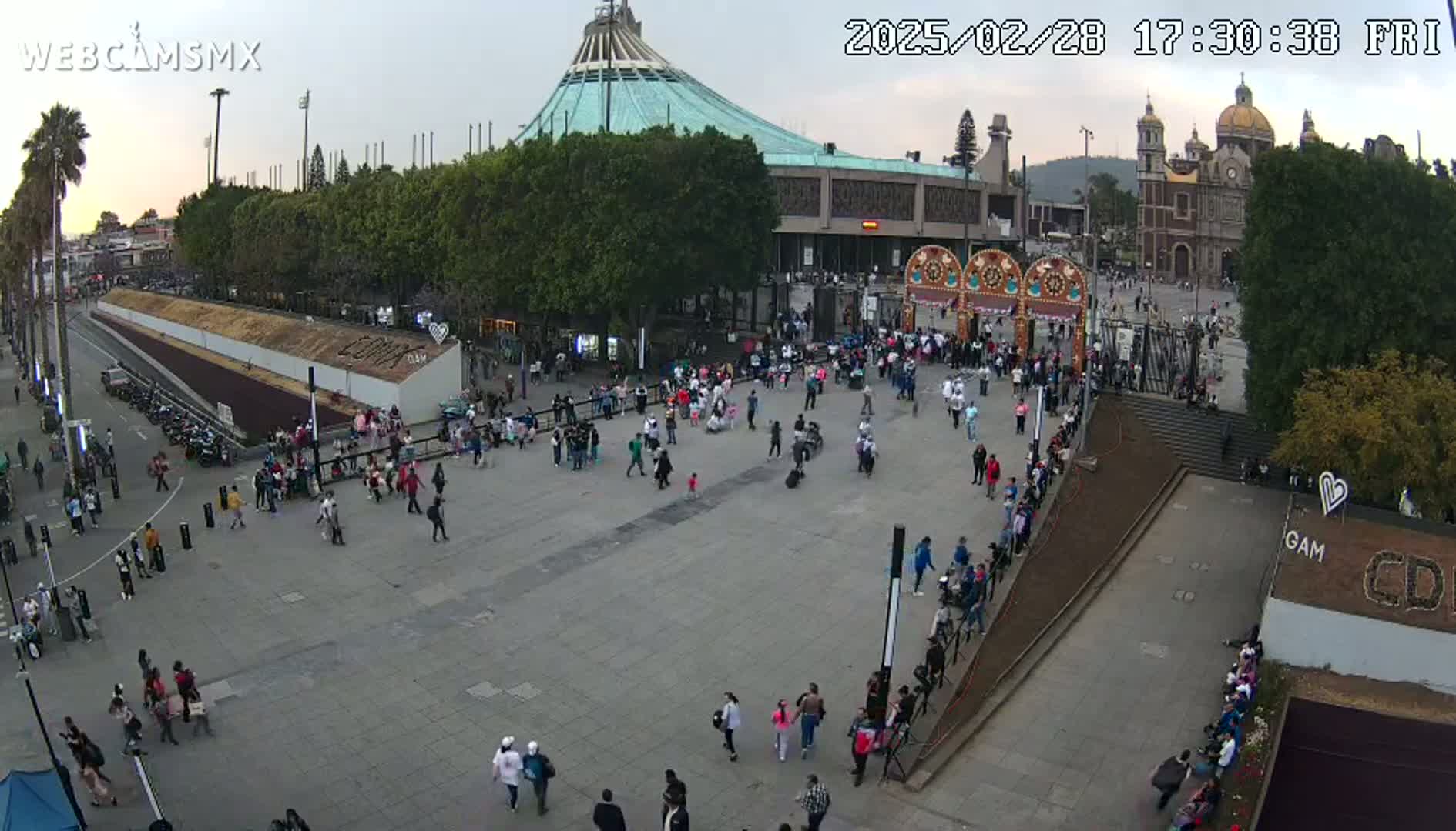 A large plaza with many people milling about in front of a large basilica under a mostly clear evening sky.