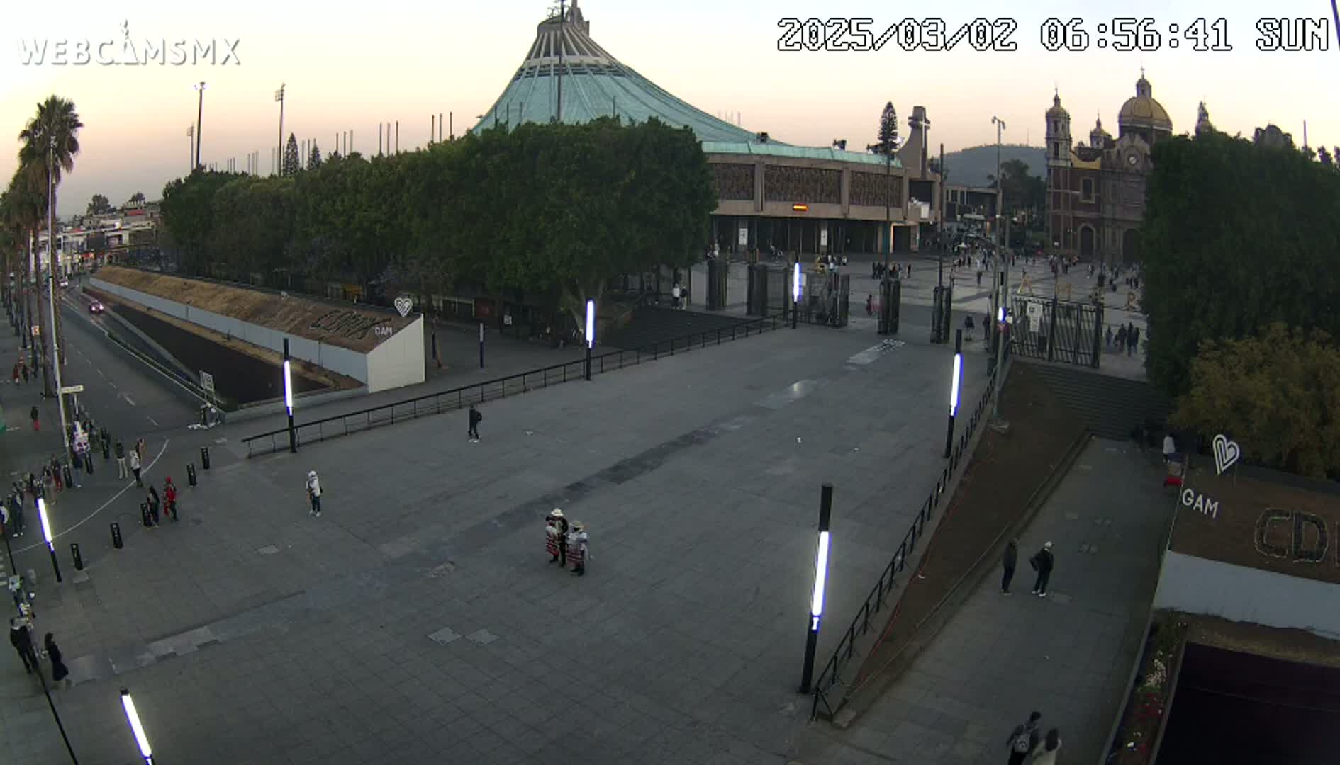 A mostly empty plaza at dusk, with a large basilica in the background, under a clear sky.