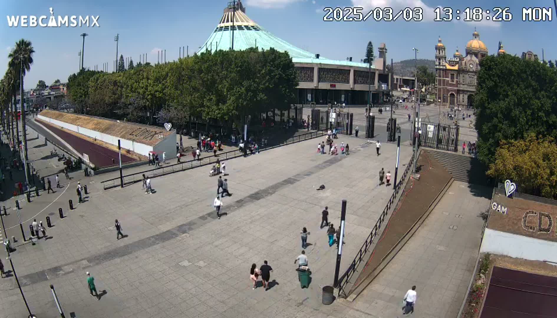 A large plaza with a few people walking around, situated in front of a large basilica under a sunny sky.