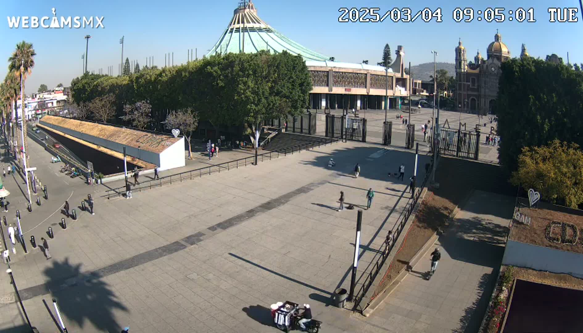 A large plaza with a basilica and a smaller church in the background on a sunny day, with a few people sparsely scattered throughout the plaza.