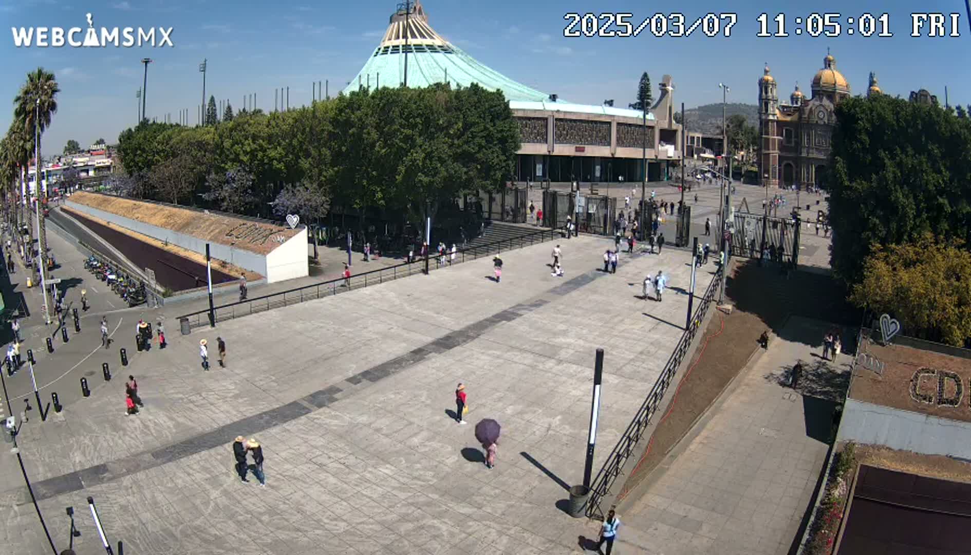 A large plaza with a few people walking around, in front of a large basilica under a clear sunny sky.