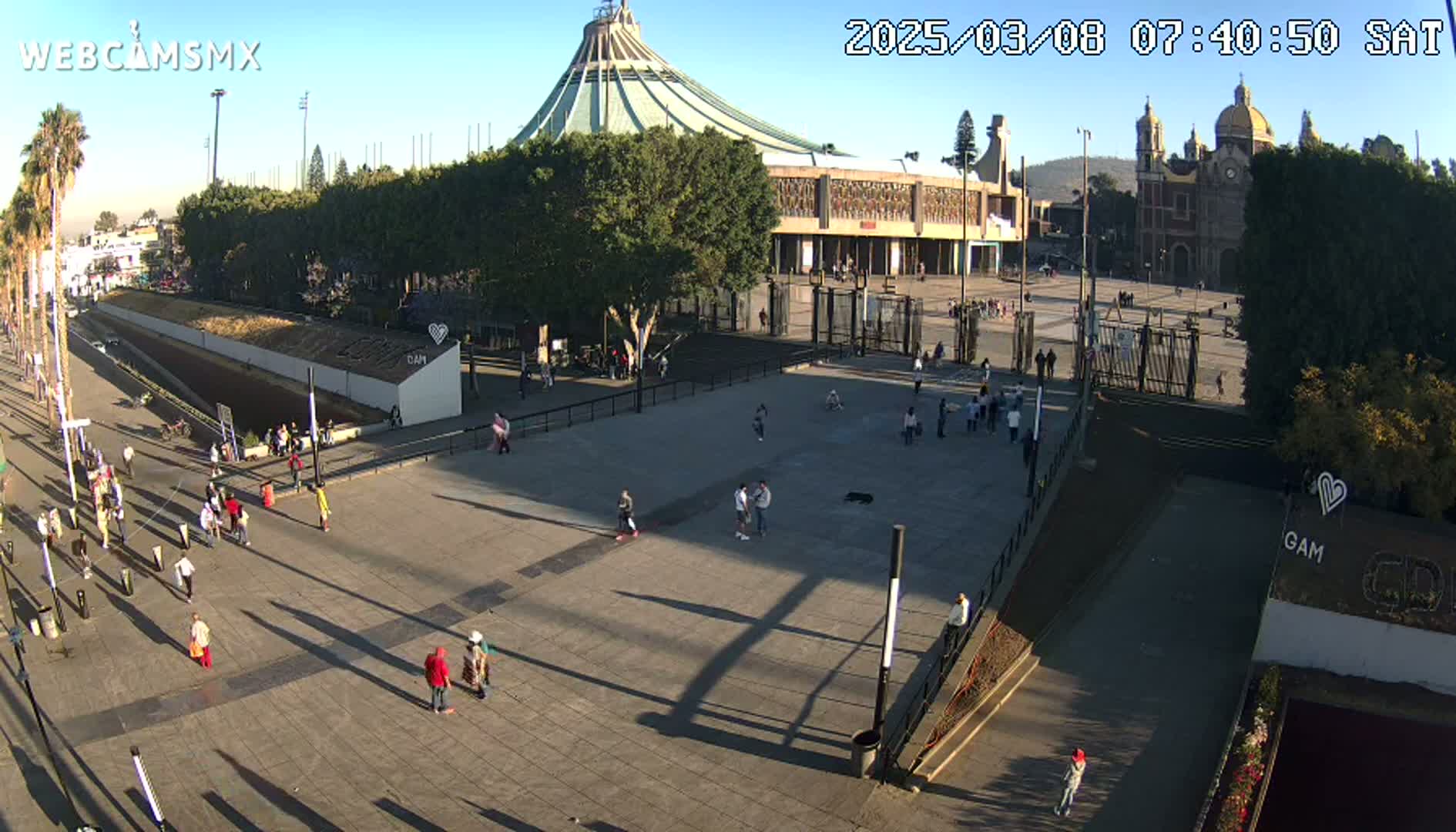 A large plaza with sparse crowds in front of a basilica under a clear, sunny sky.