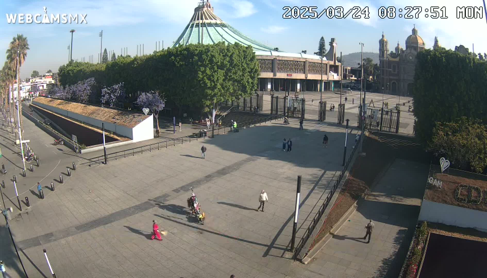 A mostly empty plaza with a large basilica and smaller church in the background on a sunny day.