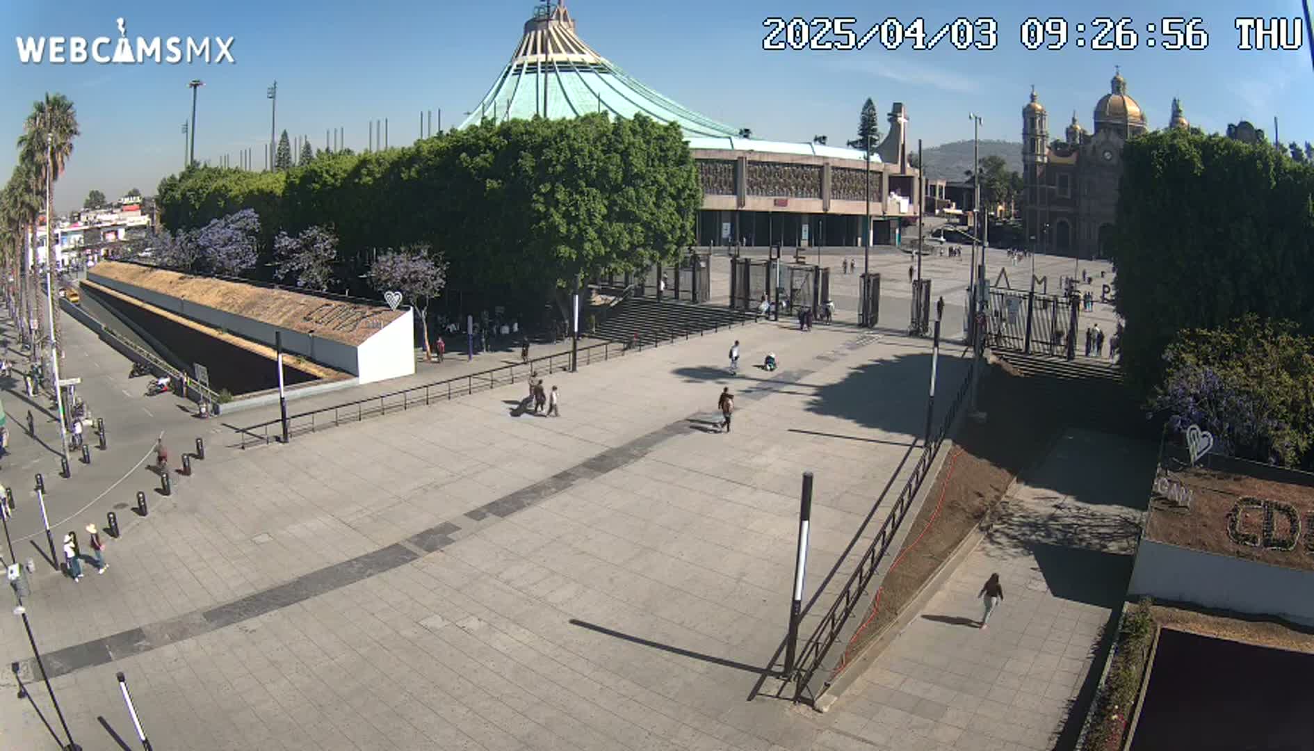 A large plaza with a basilica and several smaller buildings in the background, under a sunny sky.
