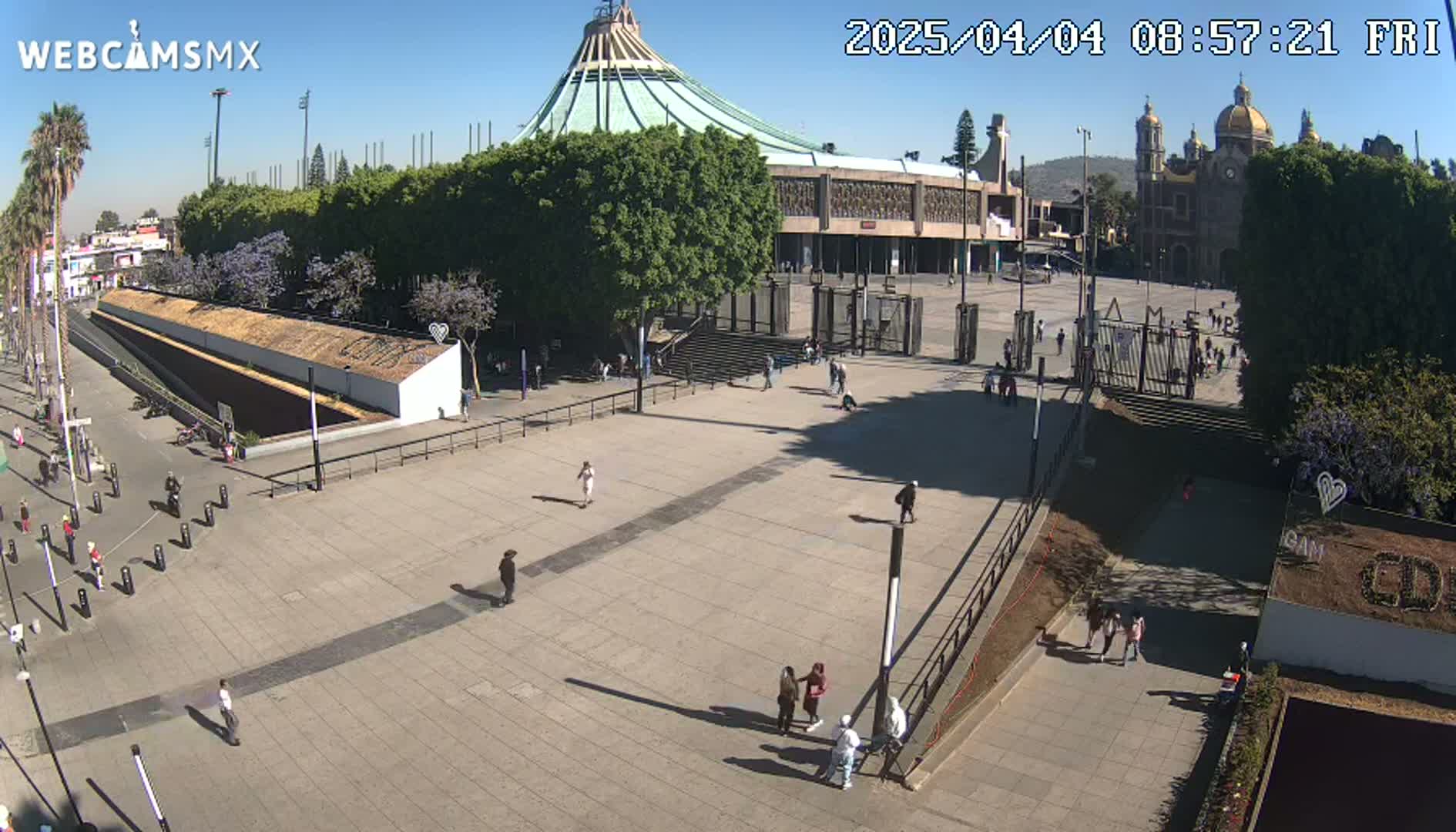 A large plaza with a few people walking around, in front of a large basilica under a clear, sunny sky.