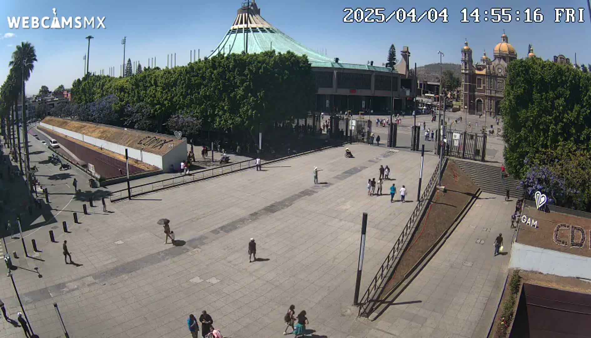 A large plaza with a few pedestrians, surrounded by buildings including a large basilica under a clear, sunny sky.