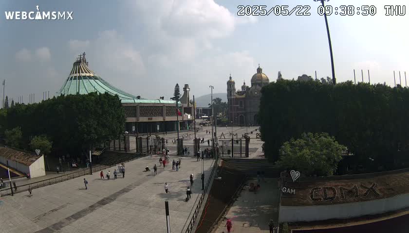 A plaza with two large churches, one modern and one traditional, is mostly empty under a partly cloudy sky.