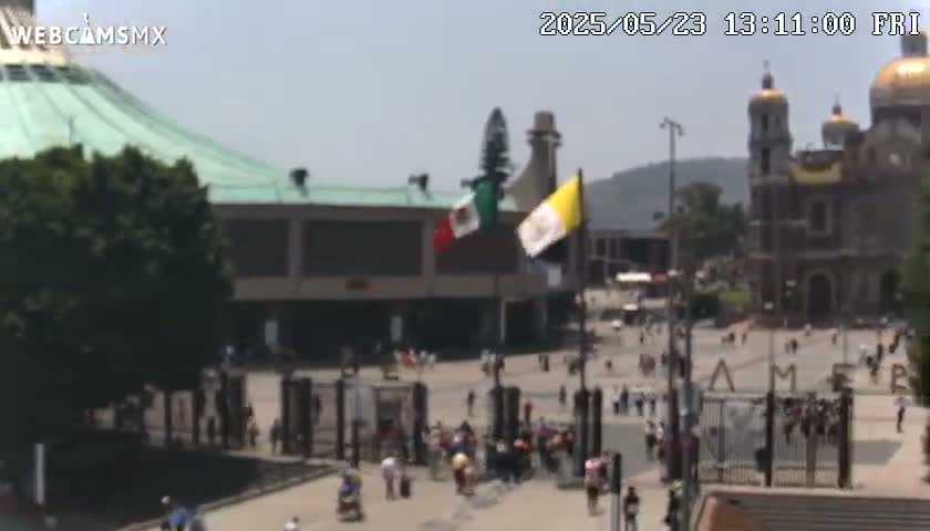 A large plaza with a crowd of people and several buildings, including a large basilica with golden domes, under a sunny sky.