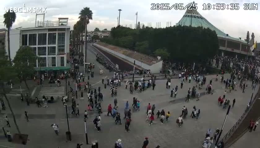 A large crowd of people gathers in a plaza on an overcast day, with a large building in the background.