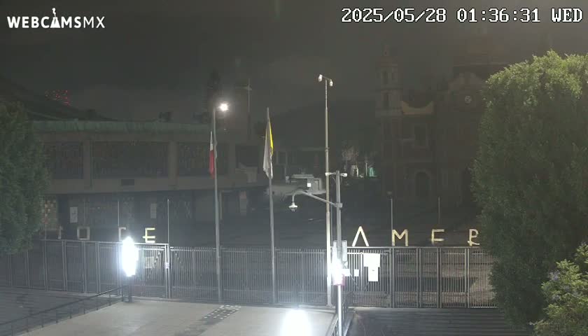 A nighttime, hazy view of a gated area with a building and several light posts, illuminated by artificial light.