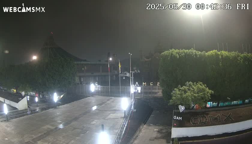 A nighttime, foggy view of a plaza or courtyard area in front of a large building, with several lights illuminating the scene.