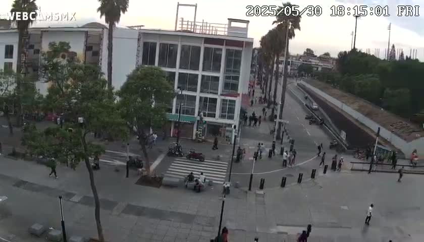 A city square with pedestrians and some vehicles, under a partly cloudy sky.