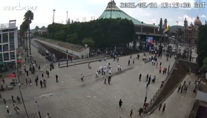 A large plaza with many people walking around, in front of a large basilica under an overcast sky.