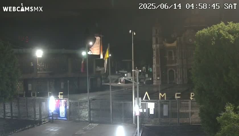 A nighttime view of a plaza or square with buildings and a gate, illuminated by artificial light.