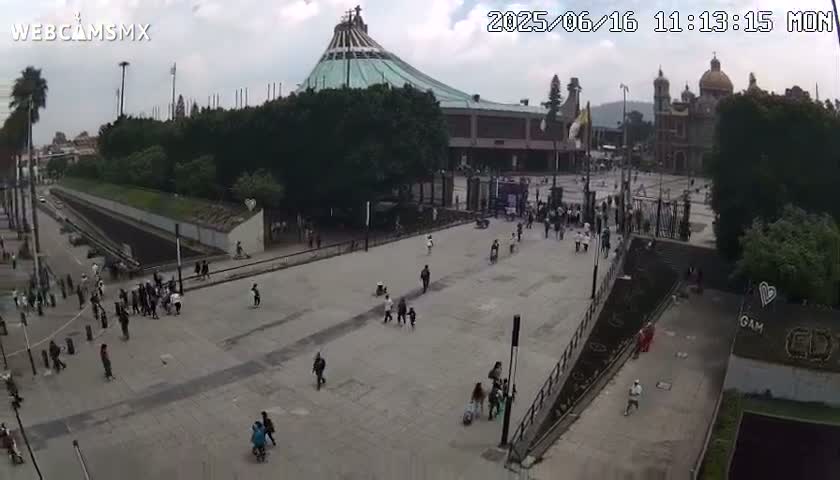 A large plaza with a few people scattered throughout and a large basilica in the background under partly cloudy skies.