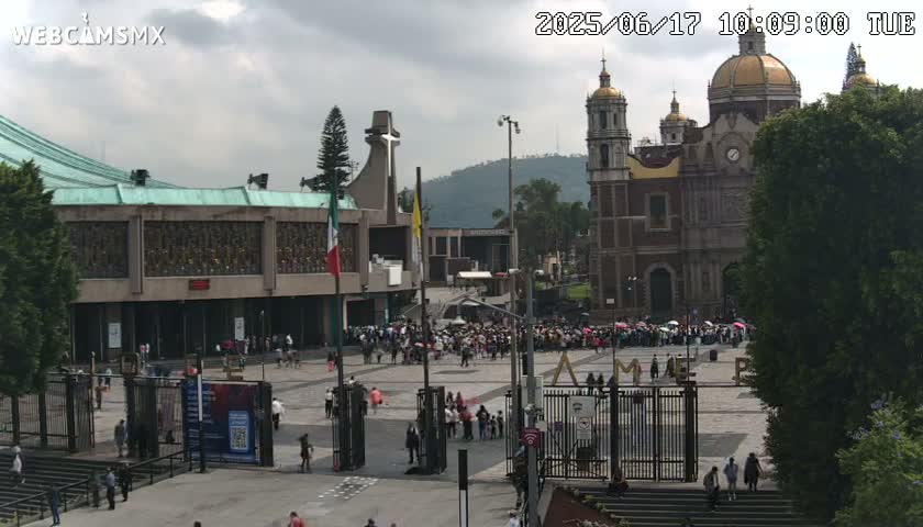 A large crowd gathers in a plaza before a basilica under an overcast sky.