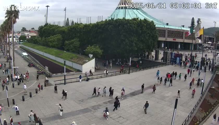 A large plaza with many people walking around, in front of a large building with a teal dome, under an overcast sky.