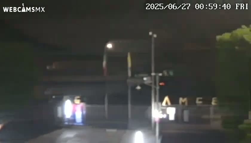 At night, a large bus is stopped at what appears to be a traffic signal, with some pedestrians visible in the background.