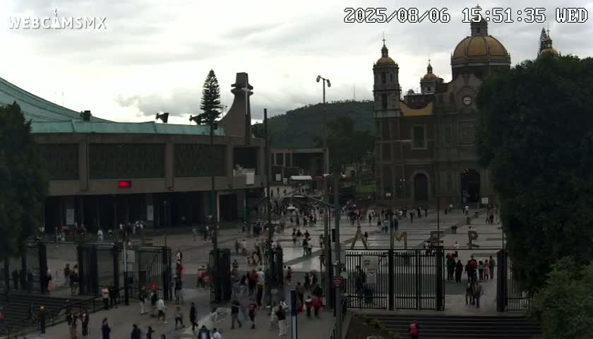 A large plaza with many people surrounds a grand basilica under an overcast sky.