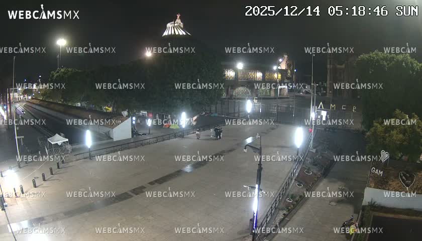 The image shows a wet, deserted urban area at night, illuminated by streetlights, with a prominent statue atop a distant building or hill under a dark, possibly overcast sky after rain.