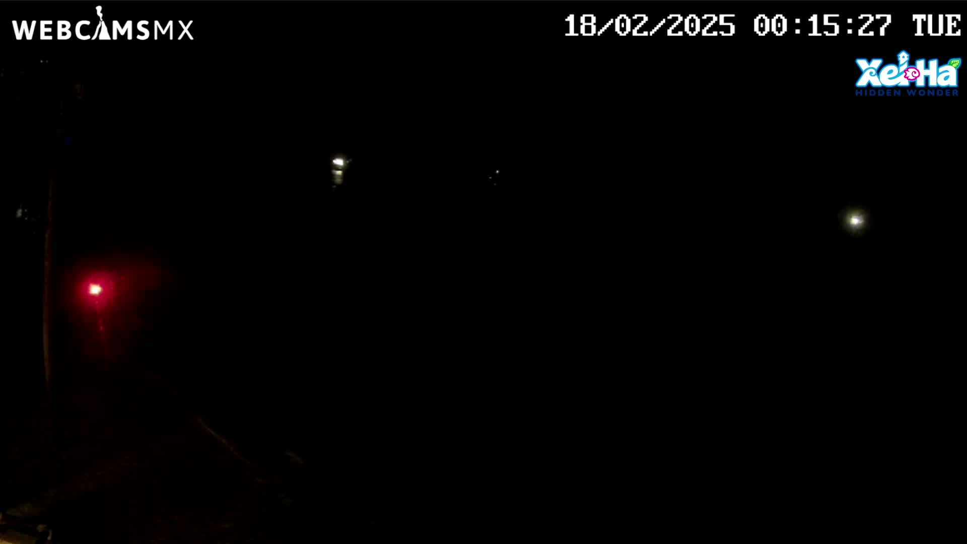 A nighttime outdoor scene shows a few distant lights and a single, closer red light in a dark, possibly foggy or hazy atmosphere.