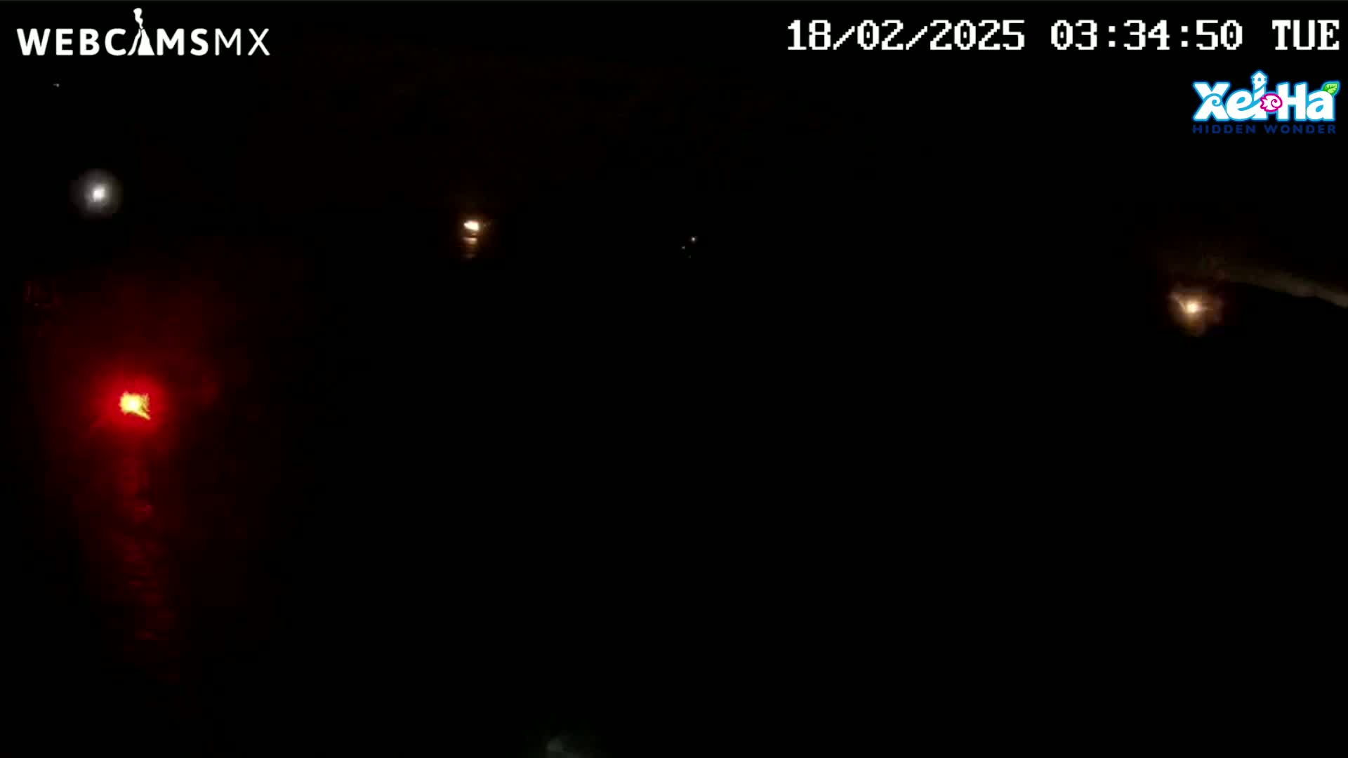 A dark nighttime scene shows several distant lights, one of which is red, against a black sky.