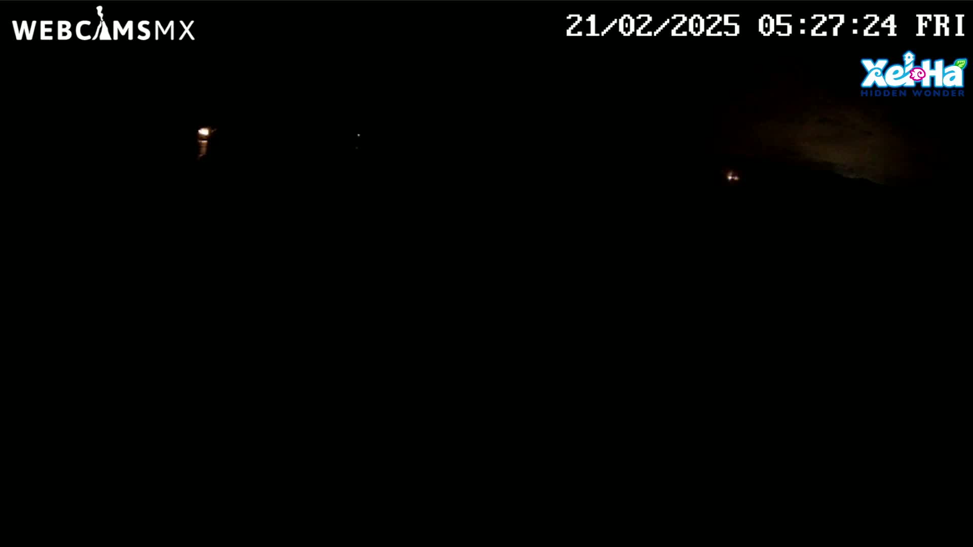 A nighttime, dark outdoor scene shows a few faint lights in the distance under a mostly clear sky.