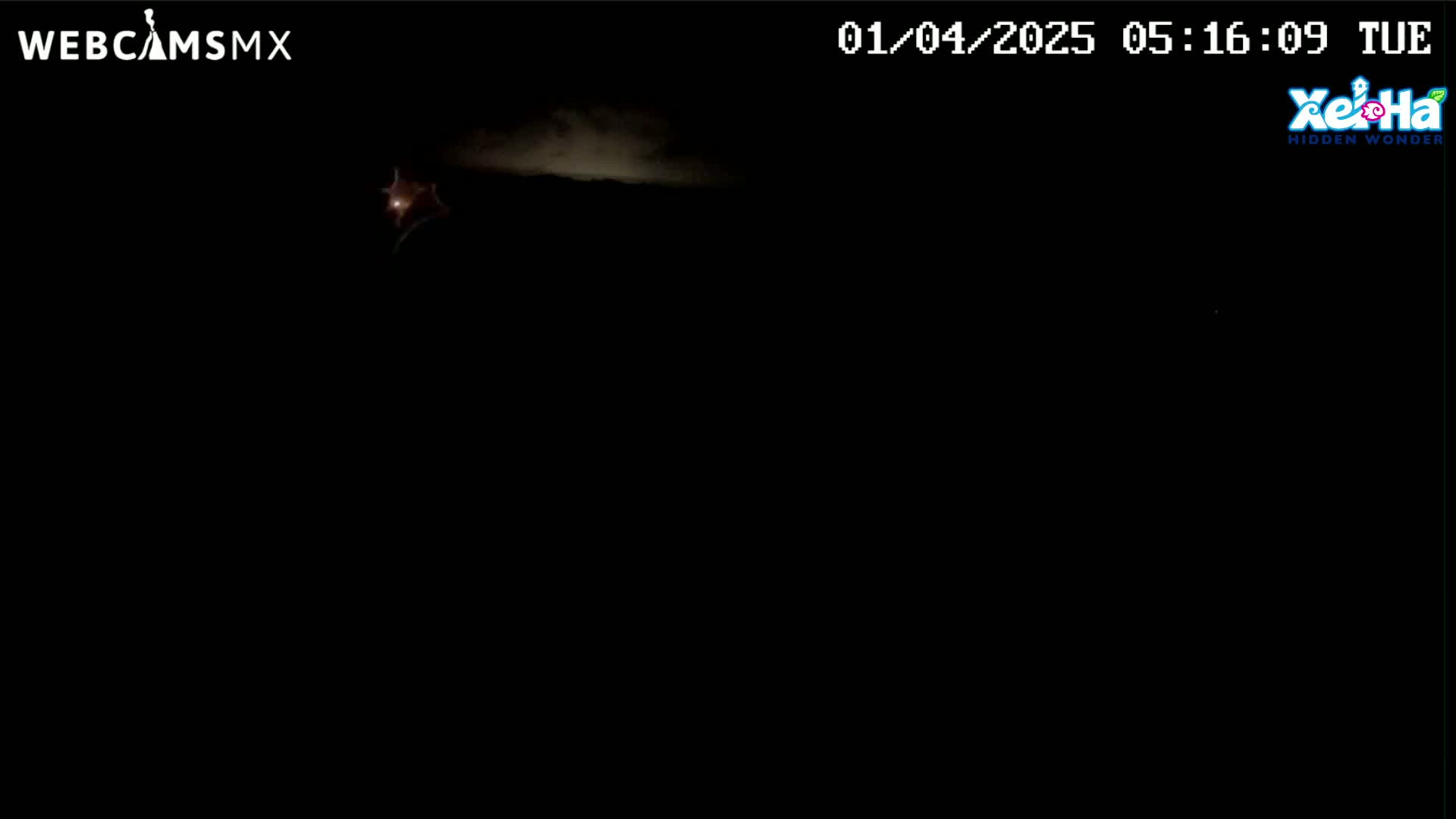 A dark, nighttime scene shows a faint, bright light in the upper left corner and a hint of clouds in the distance under a mostly dark sky.
