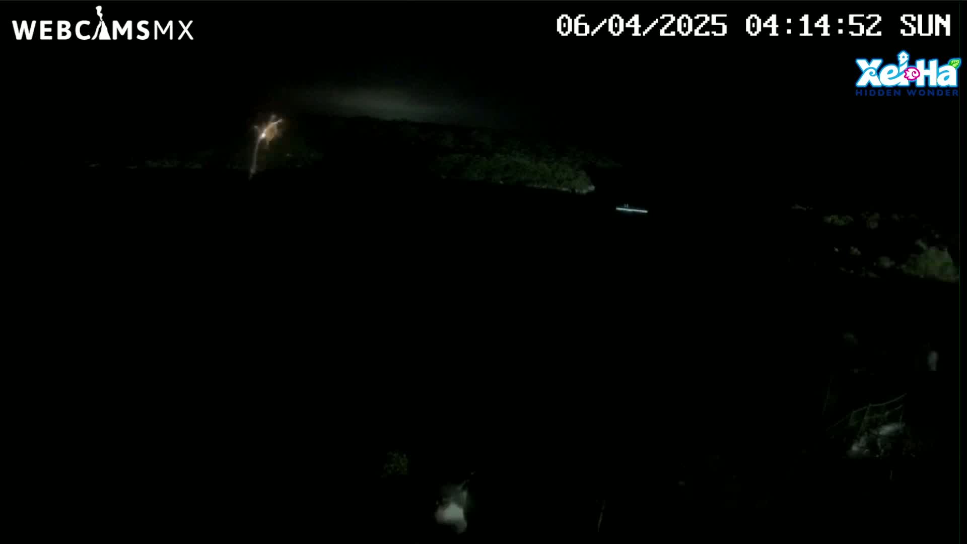 A nighttime, dark view of a body of water with a distant, dimly lit shoreline under a cloudy sky.