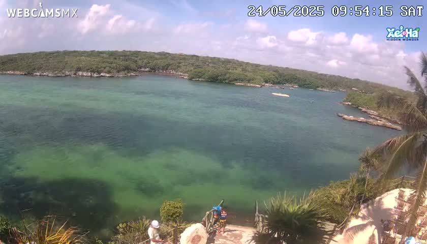 A tranquil, clear, green-tinged body of water is nestled between lush green land under a partly cloudy sky.