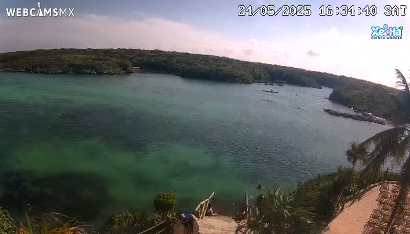A tranquil cove with clear, green water is surrounded by lush green vegetation under a partly cloudy sky.