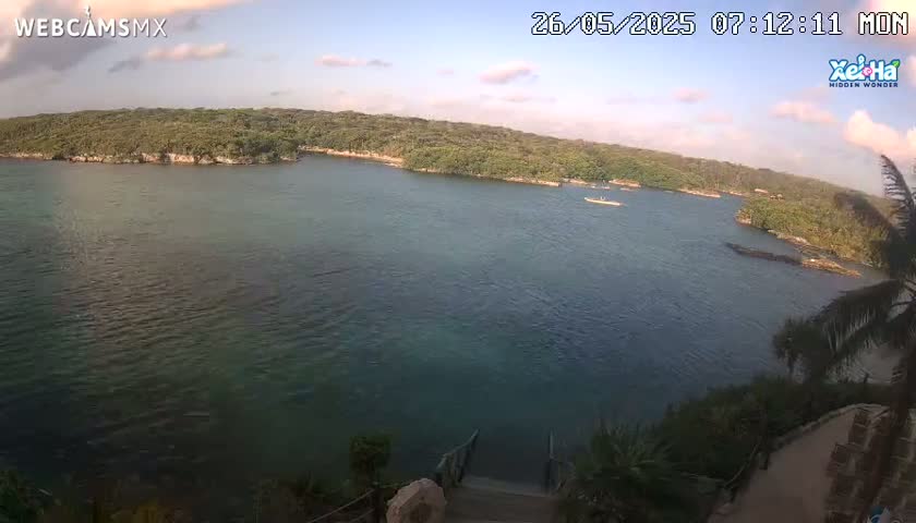 A calm body of teal water is surrounded by lush green vegetation under a partly cloudy sky.